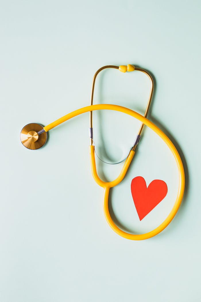 services-01 Yellow stethoscope arranged with a red heart cutout on a light green background, symbolizing heart health.